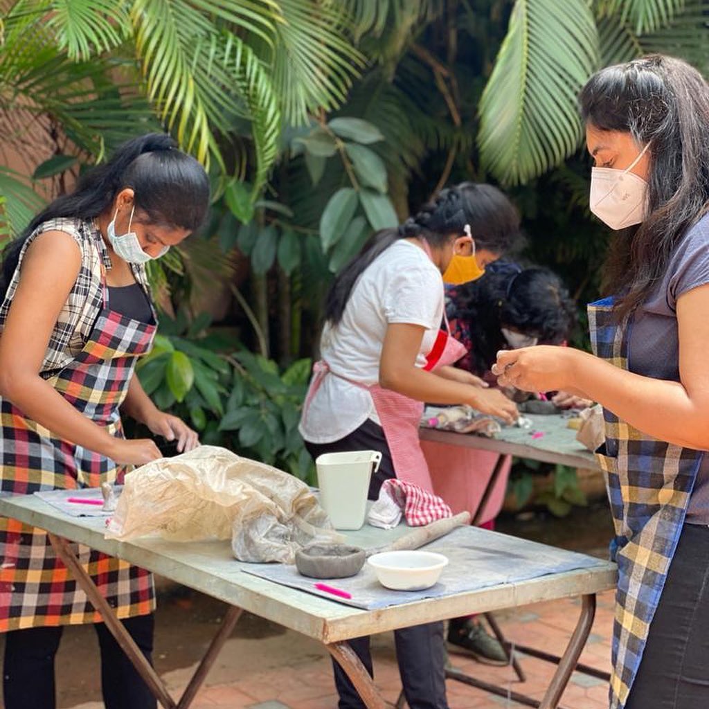 People working on pottery by hand outdoors wearing aprons.